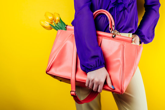 Modern and stylish look of a woman wearing spring outfit and holding a bag with yellow tulips. Studio shot