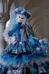 Fototapeta na wymiar Close up of woman in ornate blue and white costume, hat & mask at St Mark's Square (San Marco) during the Venice Carnival (Carnivale di Venezia)