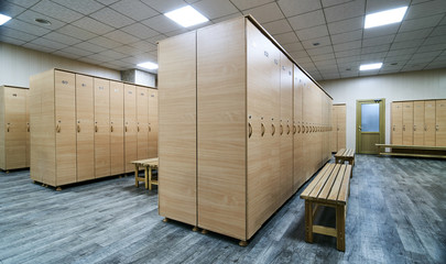 Wooden lockers with a wood bench in a locker room with doors closed. Locker room interior in modern fitness gym 