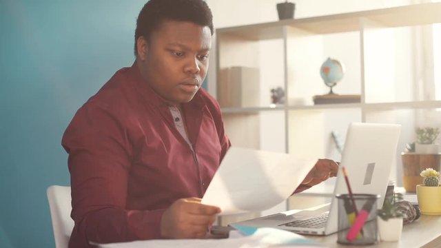 Close up face young african american man thinking and working on laptop take documents in office sunlight business internet businessman freelance looking portrait work slow motion black brainstorming