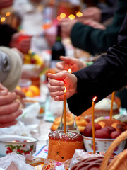 People celebrate the holy Easter. Man lights candle and protects the lightning candle from wind blowing. Candle and festive Easter roll oa table near the church before the consecration ceremony.