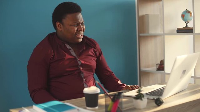 Angry young african american man use laptop in office sunlight nervous sad business internet face businessman freelance looking portrait serious work slow motion black brainstorming close up