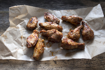 Appetizing fried pieces of chicken, pieces of chicken wings located on paper and on an old wooden background.