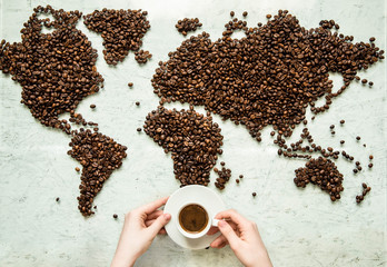 Les mains tiennent une tasse de café dans le contexte de la carte du monde à partir de grains de café