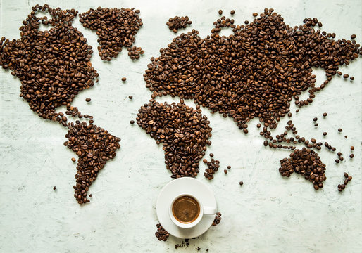 A cup of coffee on the world map which is laid out from coffee beans on a light background
