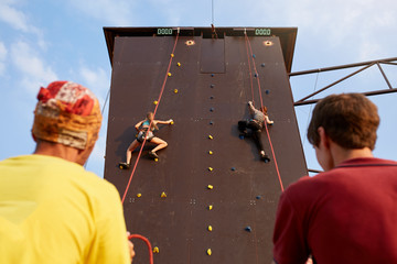 Bottom view of two young women climbers insured by men on rope belay harness approaching to...