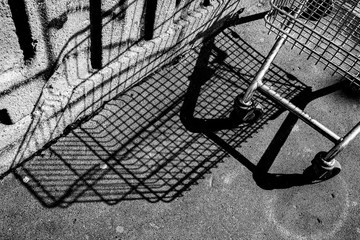 Fototapeta na wymiar Ombra e carrello del supermercato abbandonato sul marciapiede