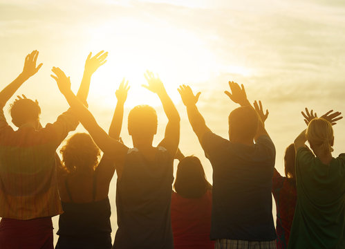 Hands Up Against Sunset Background. Bright Sunshine, People From Behind.