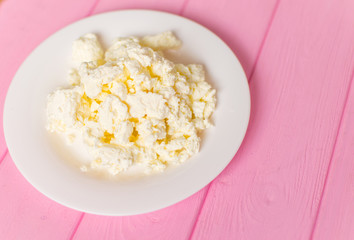 Cottage cheese on a white plate on a pink wooden background.