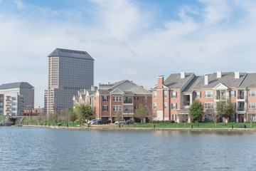 Typical condo apartment homes overlooking community lake with fountain spray. Downtown skyline in background Las Colinas, Irving, Texas, America. © trongnguyen
