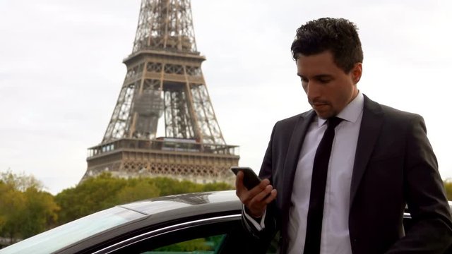 A Personal driver talking on the phone and waiting for his rich client next to the Eiffel Tower