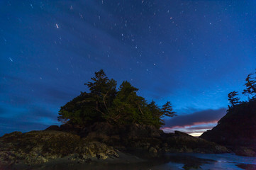 Pazifikk&uuml;ste- Pazifik Rim Provincial Park bei Tofino, Nachtaufnahme mit Sternenspuren, bewaldete Insel bei Ebbe, letztes Abendrot am Horizont, vorherschende Farbe Blau.
