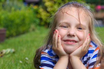 A cute 5 year old girl with wet hair lies in the grass in the garden