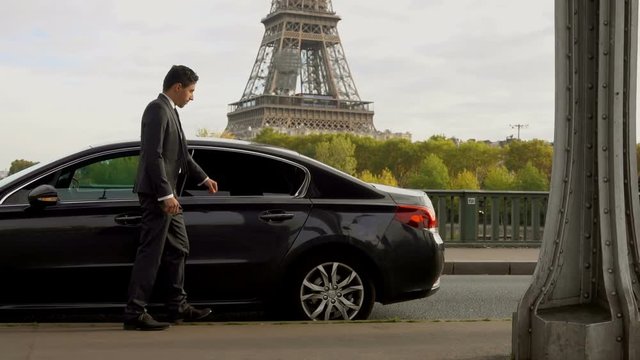 Business women with a suitcase goes and gets into the car next to the Eiffel Tower