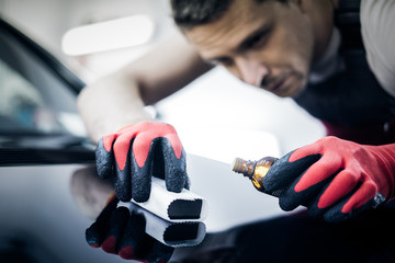 Worker on a car wash applying nano coating on a bonnet.
