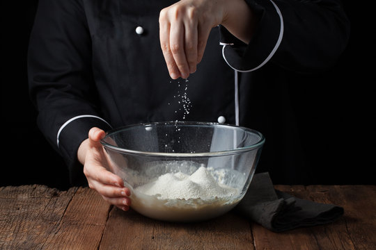 Chef Hands Sprinkles Sea Salt On Raw Dough On A Black Background, Cooking Process