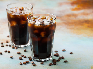 Ice coffee in a tall glass with cream poured over and coffee beans. Cold summer drink on a blue rusty background with copy space