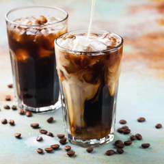 Ice coffee in a tall glass with cream poured over and coffee beans. Cold summer drink on a blue...