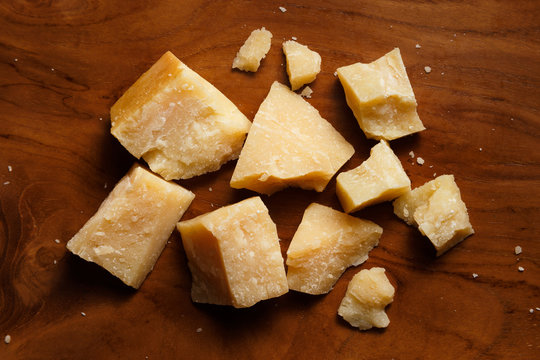 Pieces of parmesan or parmigiano reggiano cheese on a wooden board. Parmesan cheese uses in pasta, risotto and salads. Top view.