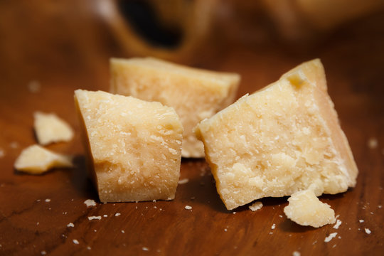 Pieces of parmesan or parmigiano reggiano cheese on a wooden board. Parmesan cheese uses in pasta, risotto and salads. Close-up.
