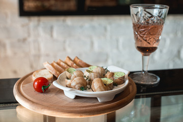 Snails with herbs butter, in traditional ceramic pan bread on a wooden plank. Glass of wine