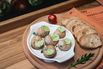 Snails with herbs butter, in traditional ceramic pan bread on a wooden plank. Glass of wine