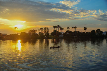 Abends am Mekong, grandiose Farbpalette beim Sonnenuntergang, Flussufer horizontal im Bild, Palmen am Ufer, kleines Boot mit zwei Fischern im Bild.