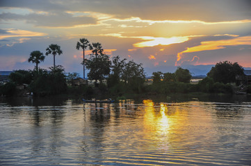 Abends am Mekong, Sonnenuntergang mit grandioser Farbpalette, Flu&szlig;ufer horizontal im Bild, linker Hand Palmen, Farben des Himmels spiegeln sich im Wasser.