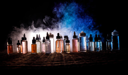 Vape concept. Smoke clouds and vape liquid bottles on dark background. Light effects. Useful as...