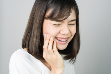 Asian girl in white casual dress Show off the toothache, Maybe because of not maintaining good oral health. on a gray background gives a soft light.