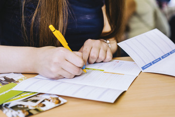 girl is writing form with yellow pen in blue shirt on the wooden table