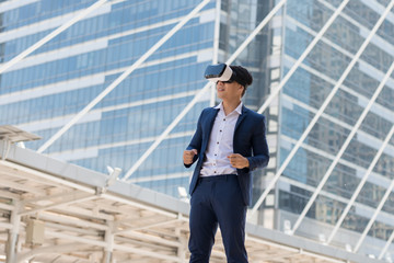 Young Asian businessman in a suit wear and virtual reality glasses. He are glad that succeed with city town background. Concept Technology and Simulation Business..