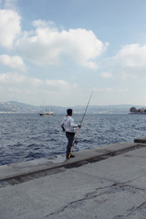 Fototapeta na wymiar Fisherman by Bosphorus strait in Tarabya area of Istanbul. Wooden yacht is in the background.
