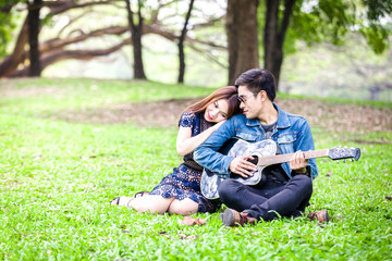 Asian couple in love playing acoustic song  guitar sitting on grass in the park