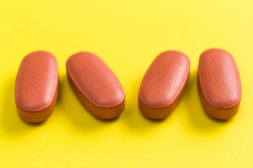 Heap of brown capsules on yellow background.