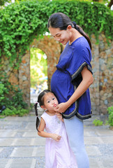 Little cute girl embracing her pregnant mother in the garden.
