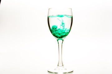 Green food coloring diffuse in water inside wine glass with empty copyspace area for slogan or advertising text message, over isolated white background.