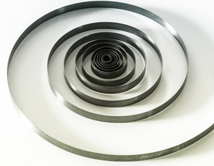 Spiral steel spring on a white mirror surface close-up.