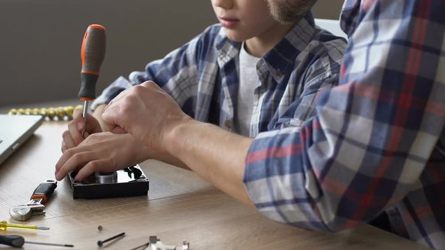 Boy using screwdriver to repair hard disk, father teaching, giving some advice