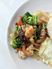Vegetable stir-fry dish with Thai healthy food stir-fried broccoli, mushroom, carrot, hearb, squid and shrimp with rice and fried egg in white plate on white background.  Thai style fast food can orde