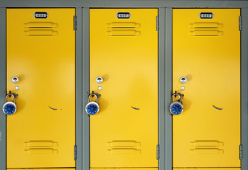 Yellow school lockers with locks - Three locker doors of three yellow lockers in the hallway of a...