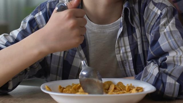 Boy reluctantly mixing cornflakes with spoon, upset child, loss of appetite