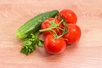 Tomatoes on branch, cucumber and parsley on a wooden surface
