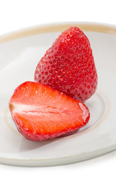 Whole and half of garden strawberry fruit on saucer closeup