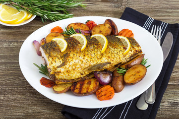 Baked carp with vegetables grilled on a white plate on a wooden background.