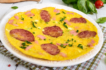 Omelette with ham, salami, cheese and greens on a plate on a white wooden background. Breakfast.