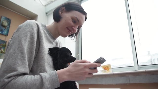 Young girl taking selfie with cute black pet chihuahua lap dog in living room