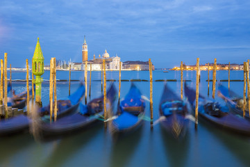 Romantic colorful night view on the lagoon of Venice at sunset during blue hour with moving gondolas and San Giorgio Maggiore church and campanile in the background