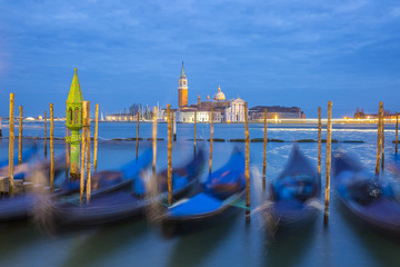 Romantic colorful night view on the lagoon of Venice at sunset during blue hour with moving gondolas and San Giorgio Maggiore church and campanile in the background