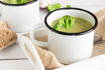Broccoli soup served in rustic mug on a sack, decorated with fresh vegetable on top.